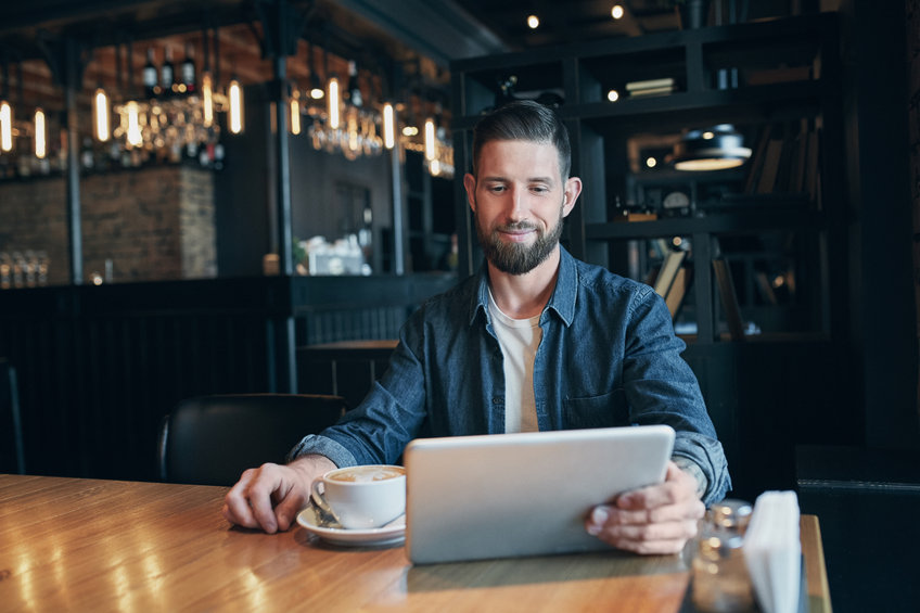 oung man drinking coffee in cafe and using tablet to read about Ethereum transaction fees.