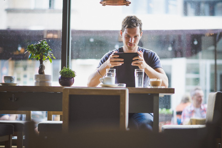 Young man checking bitcoin futures activity tablet in cafe