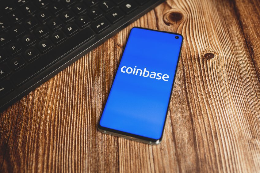 Picture of a smartphone with the bluie Coinbase app open on a wooden desk and a keyboard in the background.