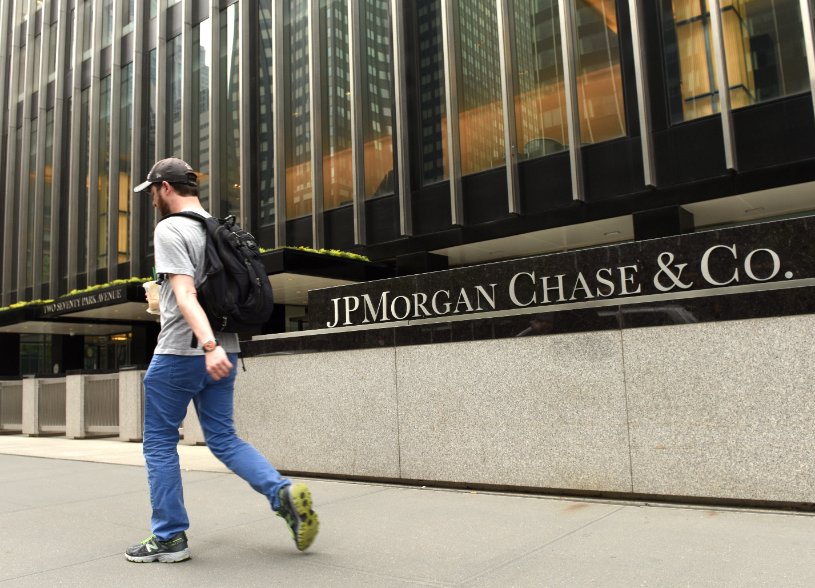 Young adult walking in front of a JPMorgan office on Wall Street.