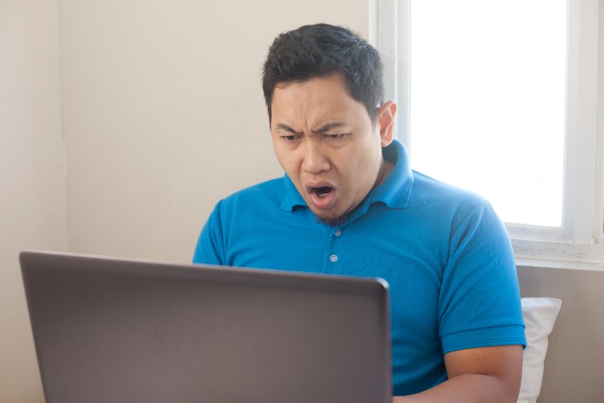Man looking stunned at a laptop in front of a backlit window.