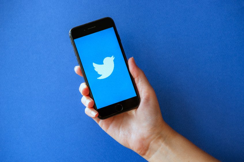 Image of a hand holding a smartphone with Twitter's logo on it, in front of a deep blue background.