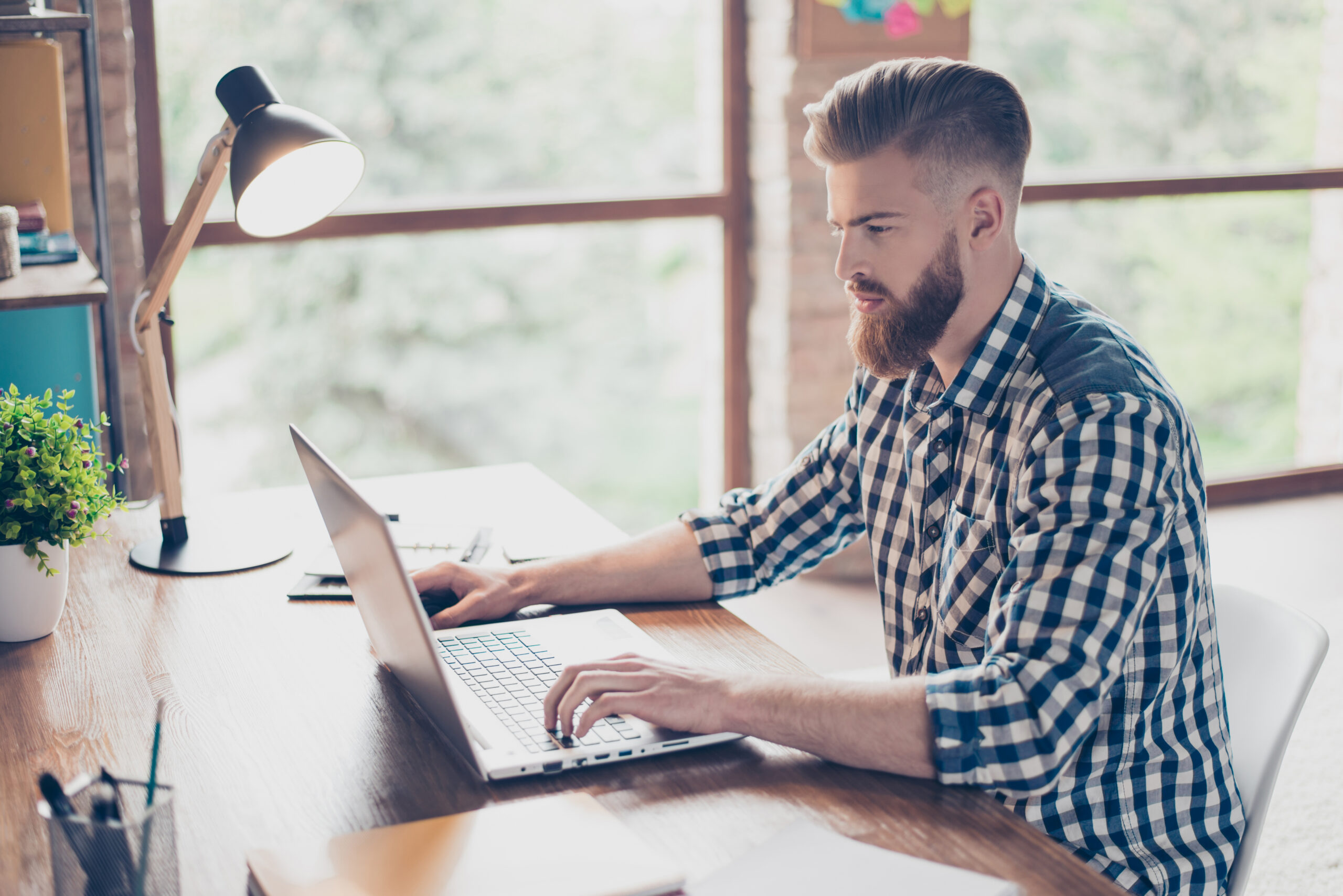Image of a man looking at a laptop seriously in front of a window.