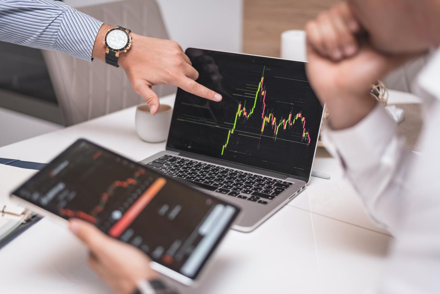 An image of two traders looking at cryptocurrency charts on a laptop and a tablet