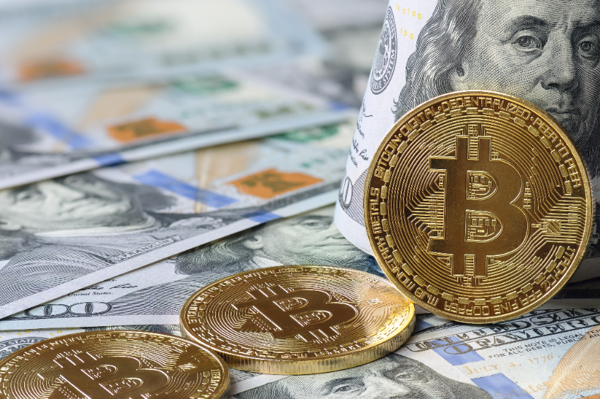 Three bitcoins sitting on top of $100 USD notes.