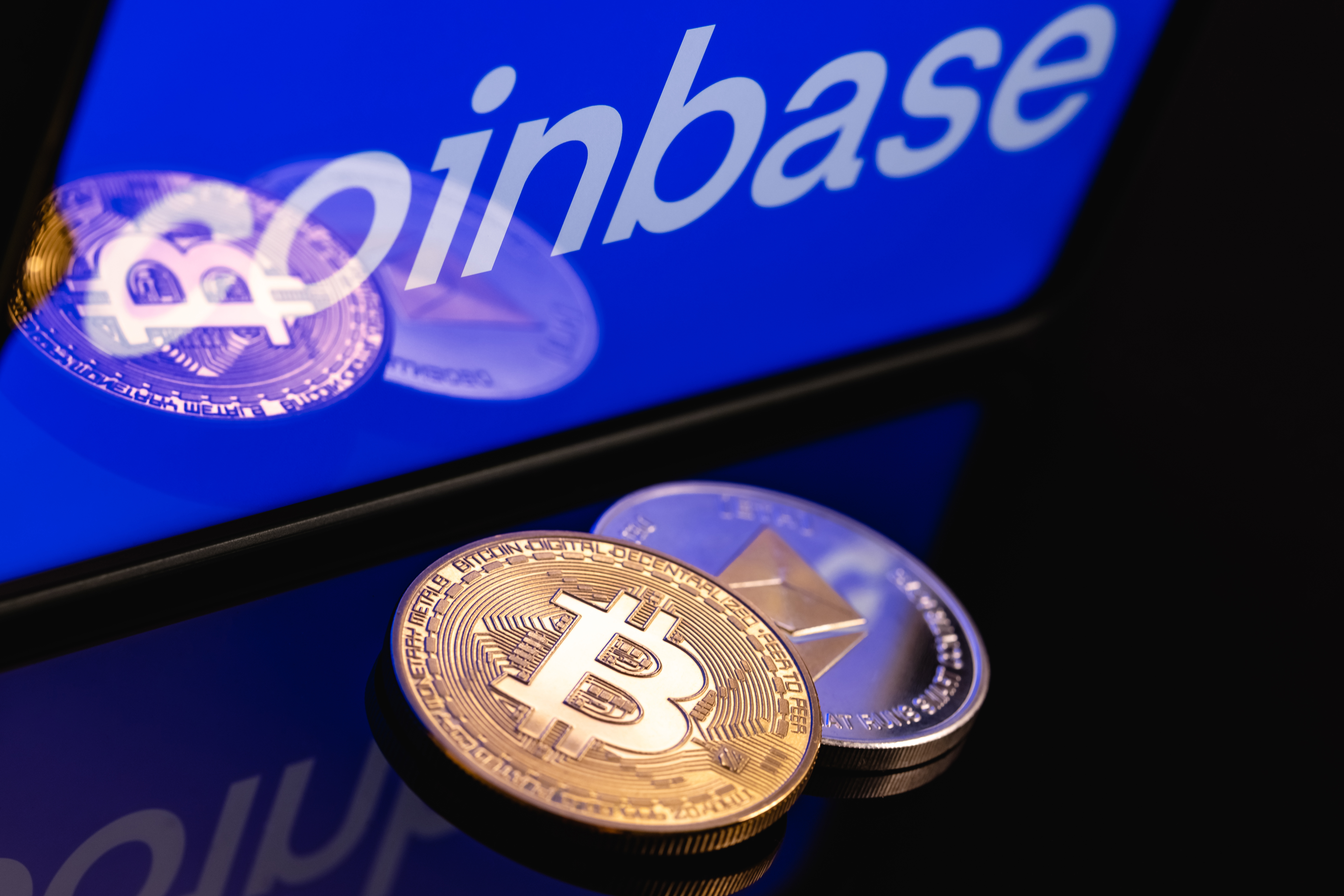 Coinbase logo on a phone screen above one representation of BTC and one of ETH signifying that the lawsuits concerns a patent used for crypto transactions