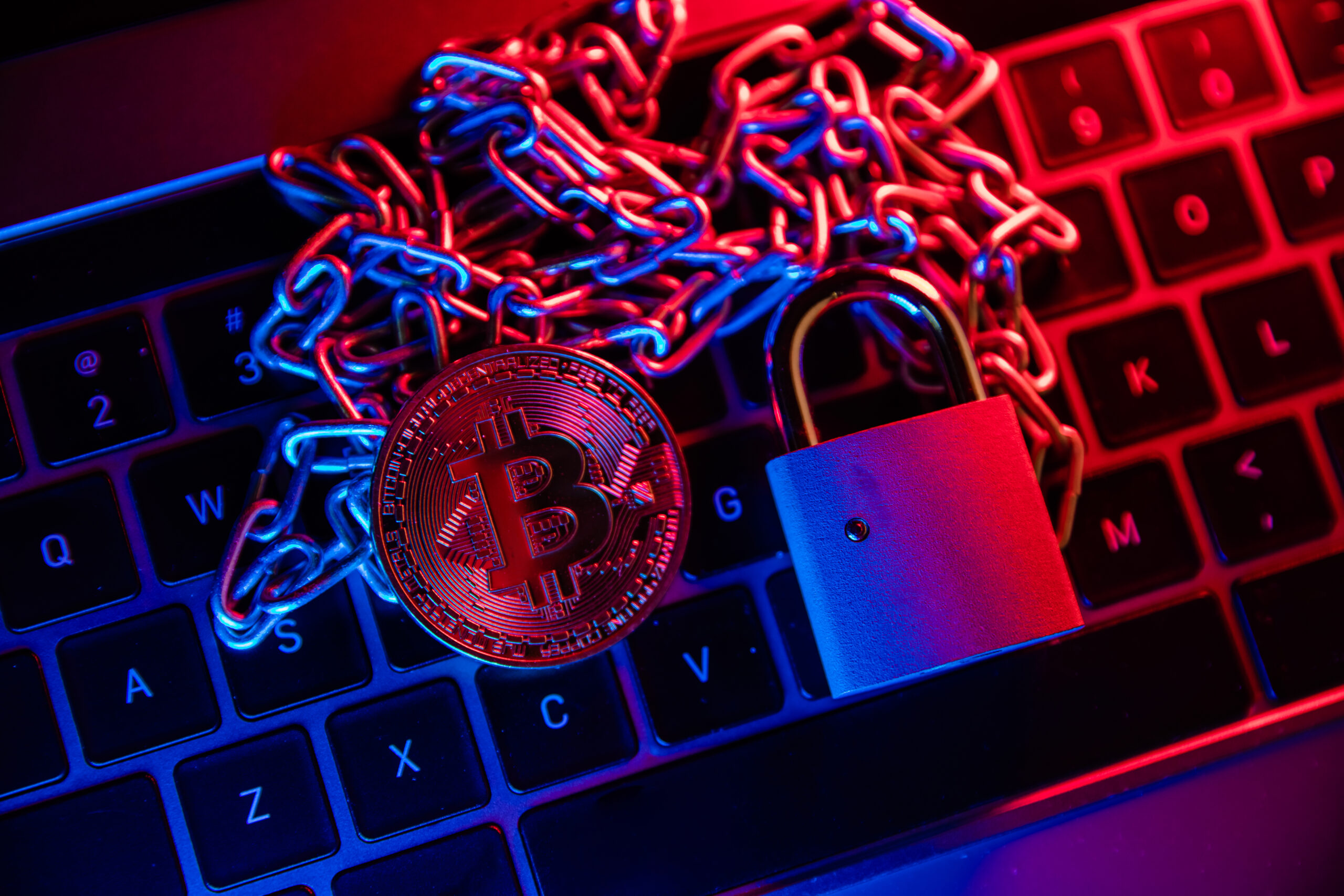 A BTC gold coin on a keyboard, chained with a padlock attached
