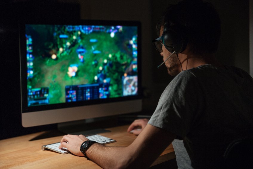 Back view of concentrated young crypto gamer in headphones and glasses