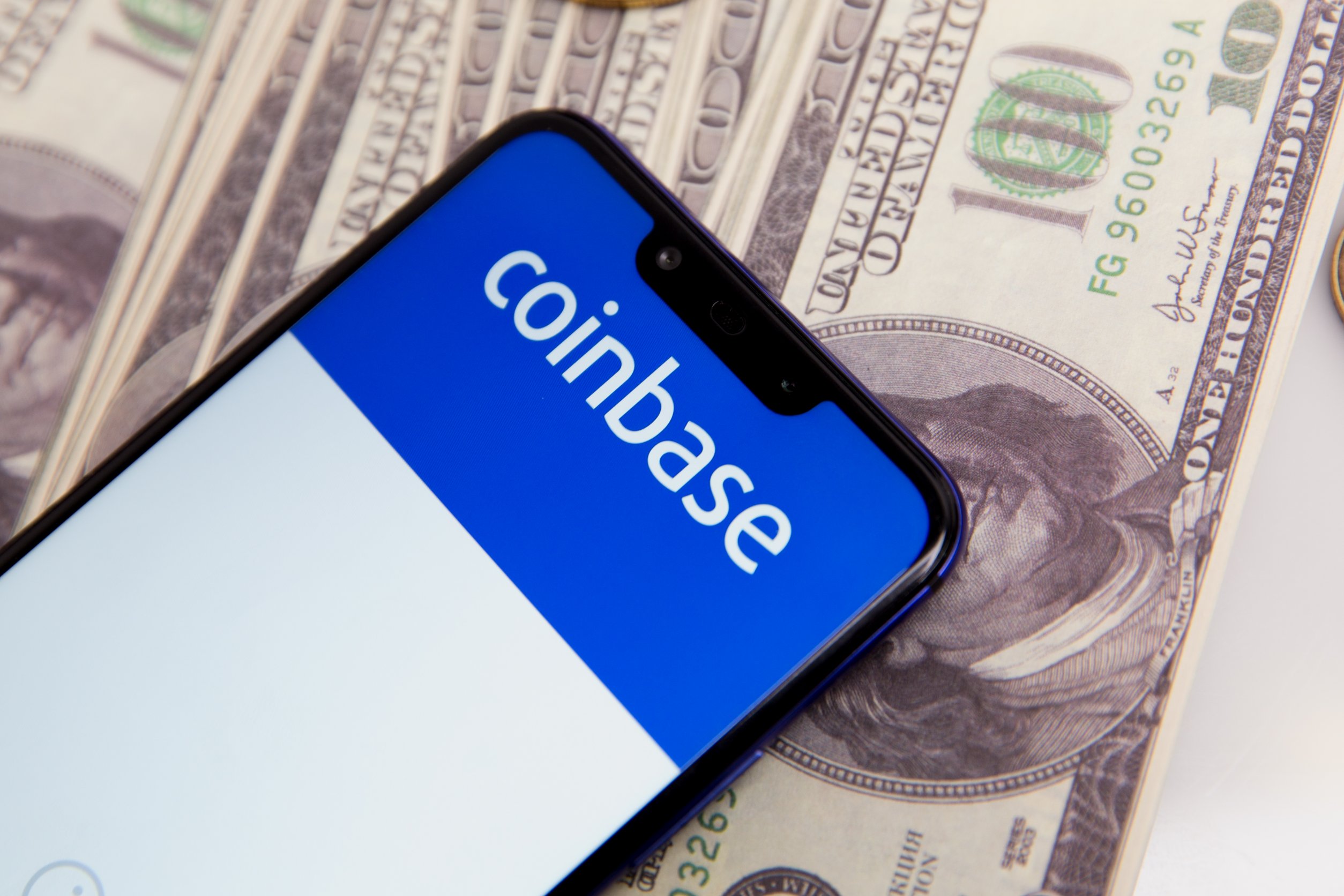 Phone screen with 'COINBASE" on it on top of a pile of cash.