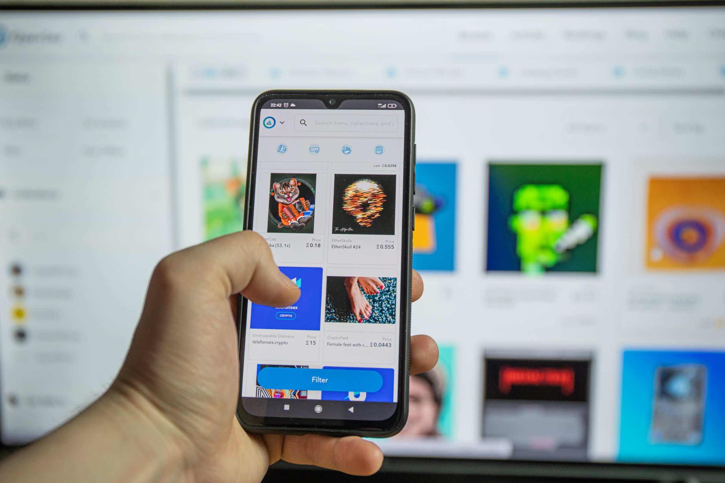 A phone screen showing NFTs in front of a bigger, blurred screen also showing NFTs.