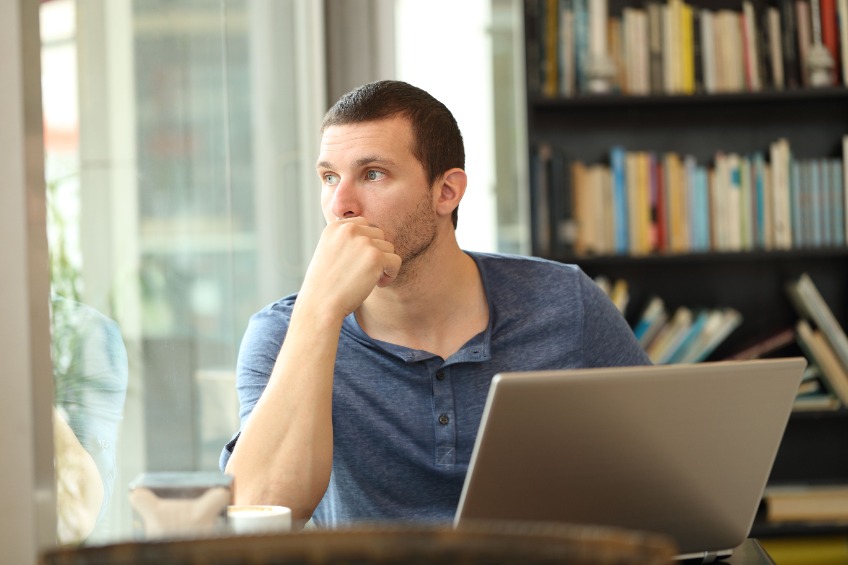 Pensive man using laptop looking outdoors through a window in a coffee shop