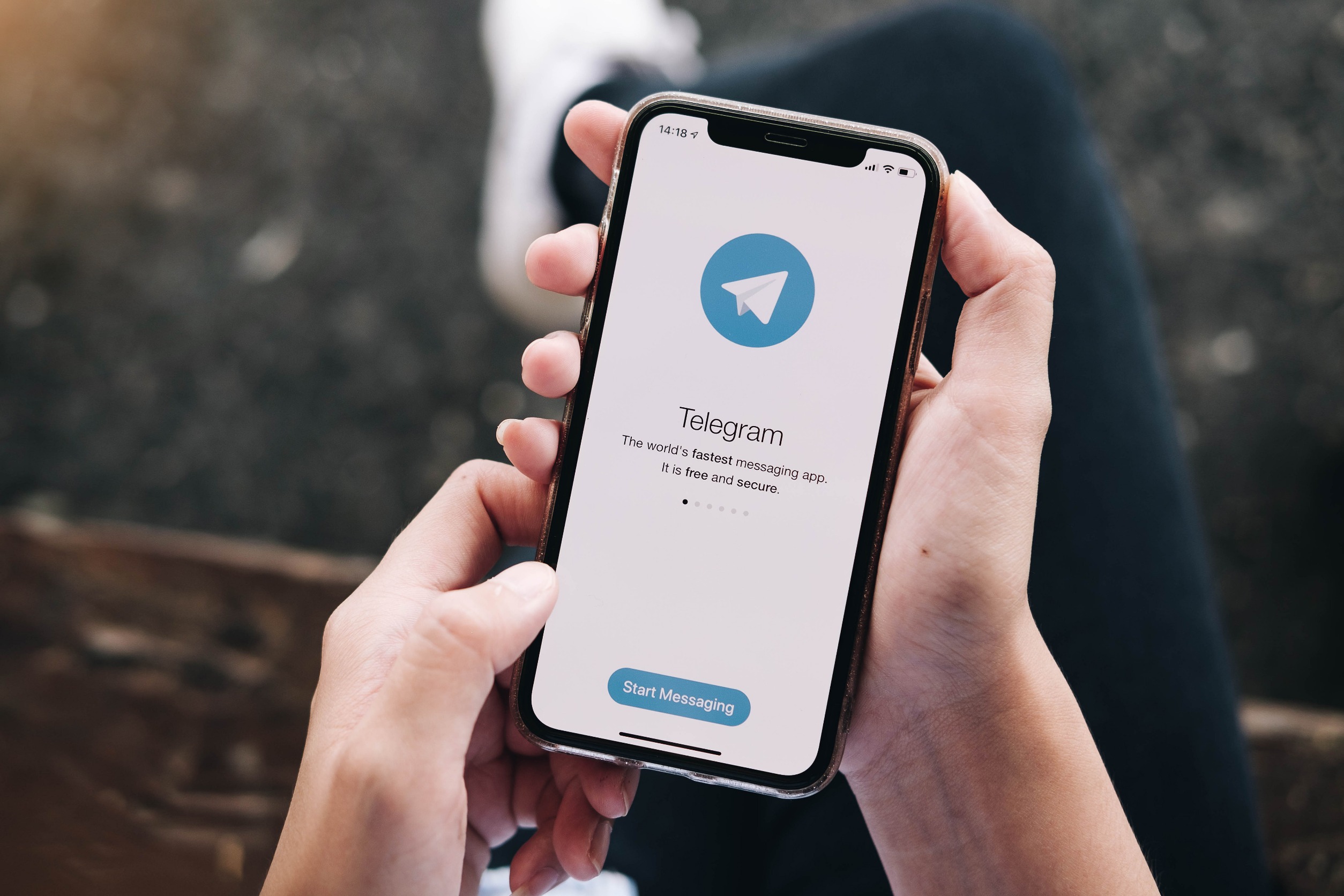 Hands holding a phone with the Telegram logo/loading screen on the screen.