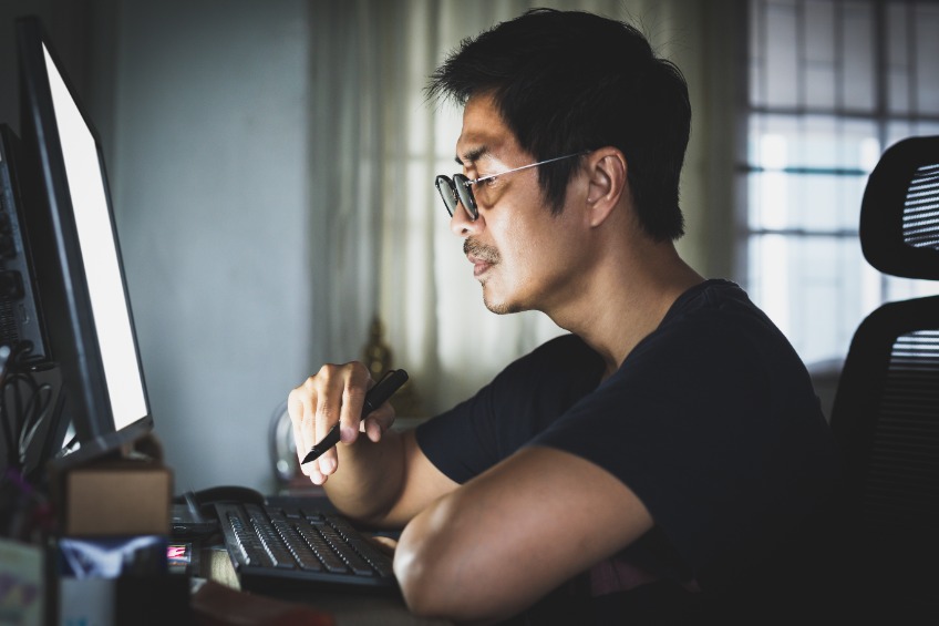Man wearing t shirt working on computer at home late at night.