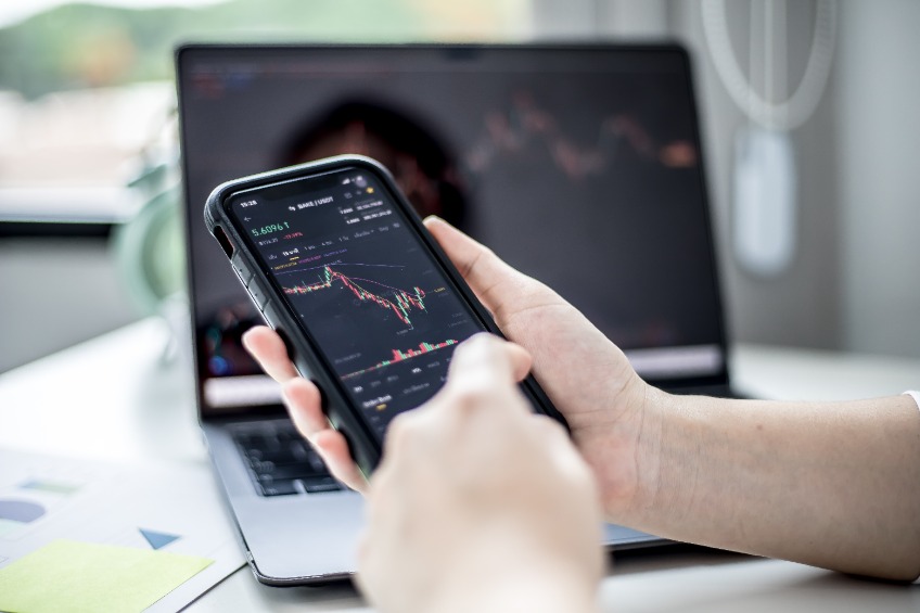 Stock investors hold a phone, open a stock chart viewer to read stock price charts, analyze purchases.