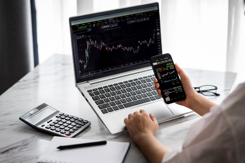 Hand holding smartphone with stock market data and using laptop display graph