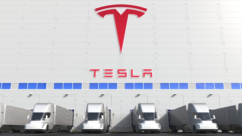 Electric semi-trailer trucks at warehouse loading bay with TESLA logo on the wall.