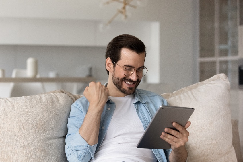 Overjoyed young Caucasian man look at tablet triumph get pleasant good email or message online.