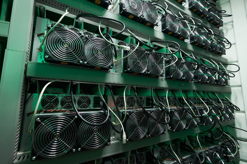 Bitcoin miners in large farm. ASIC mining equipment on stand racks mine cryptocurrency in steel container.