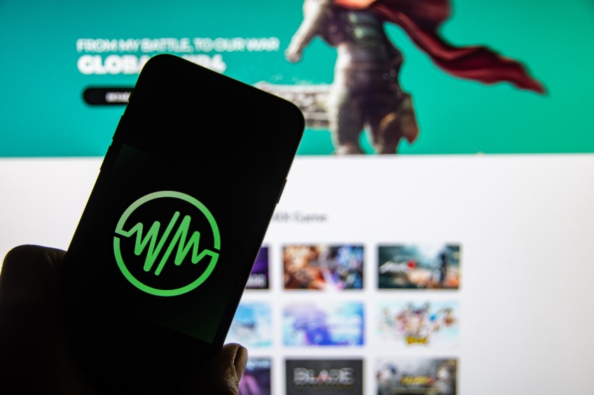 The logo of the cryptocurrency "Wemix" on the display of a smartphone in front of the website