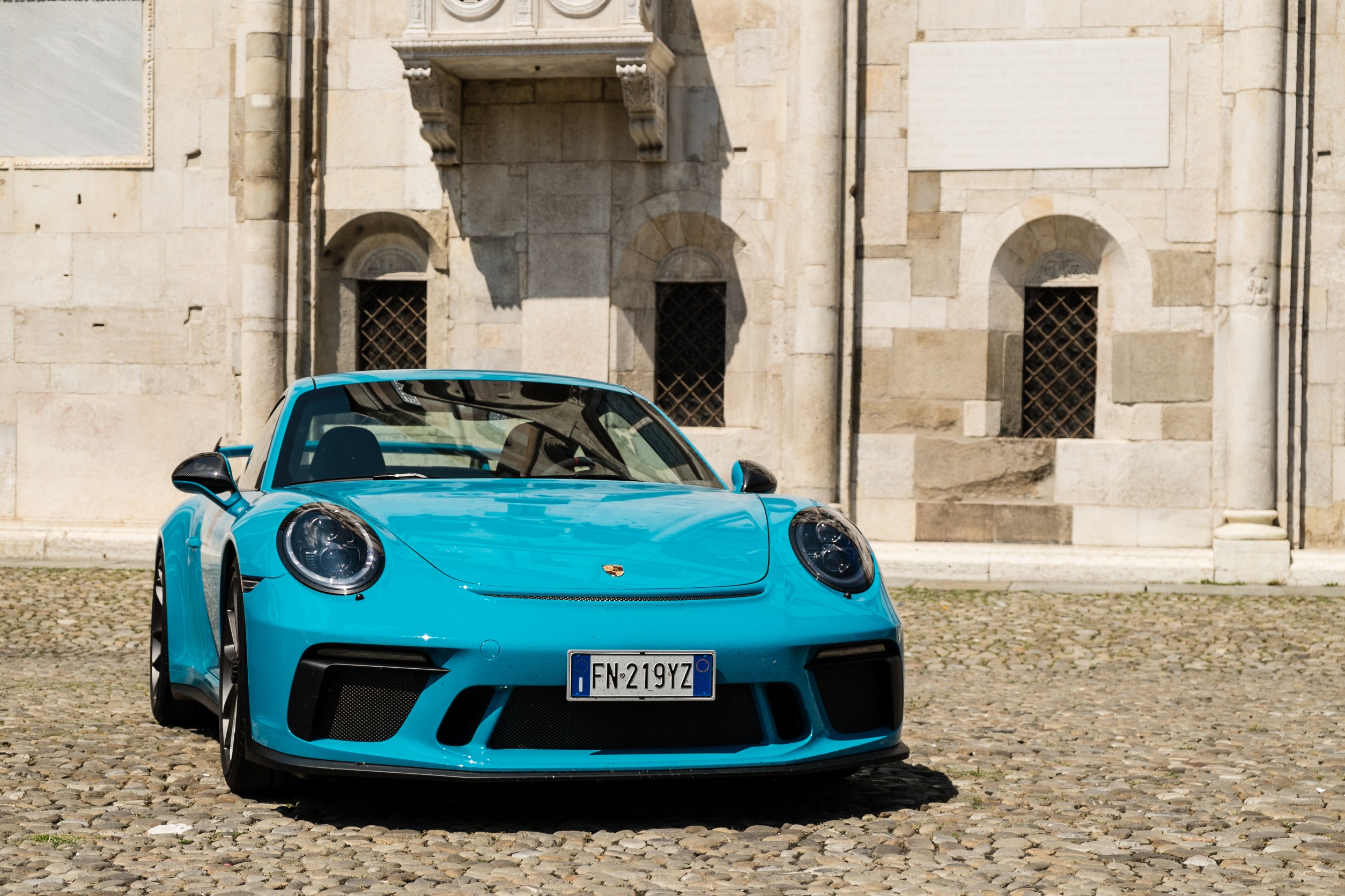 A cyan Porsche 911 in front of a historic building.