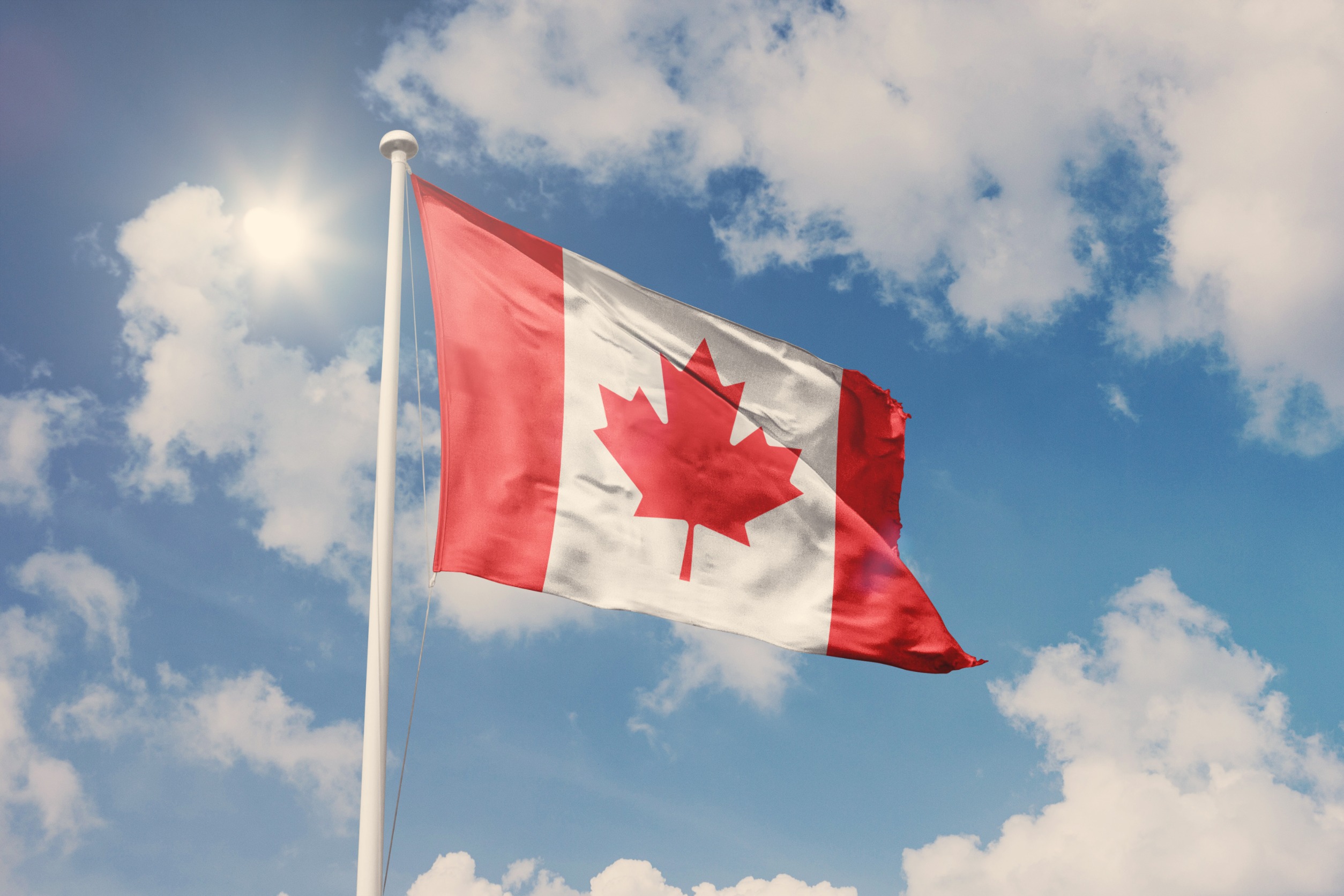 Canadian flag waving in the wind against a blue sky.