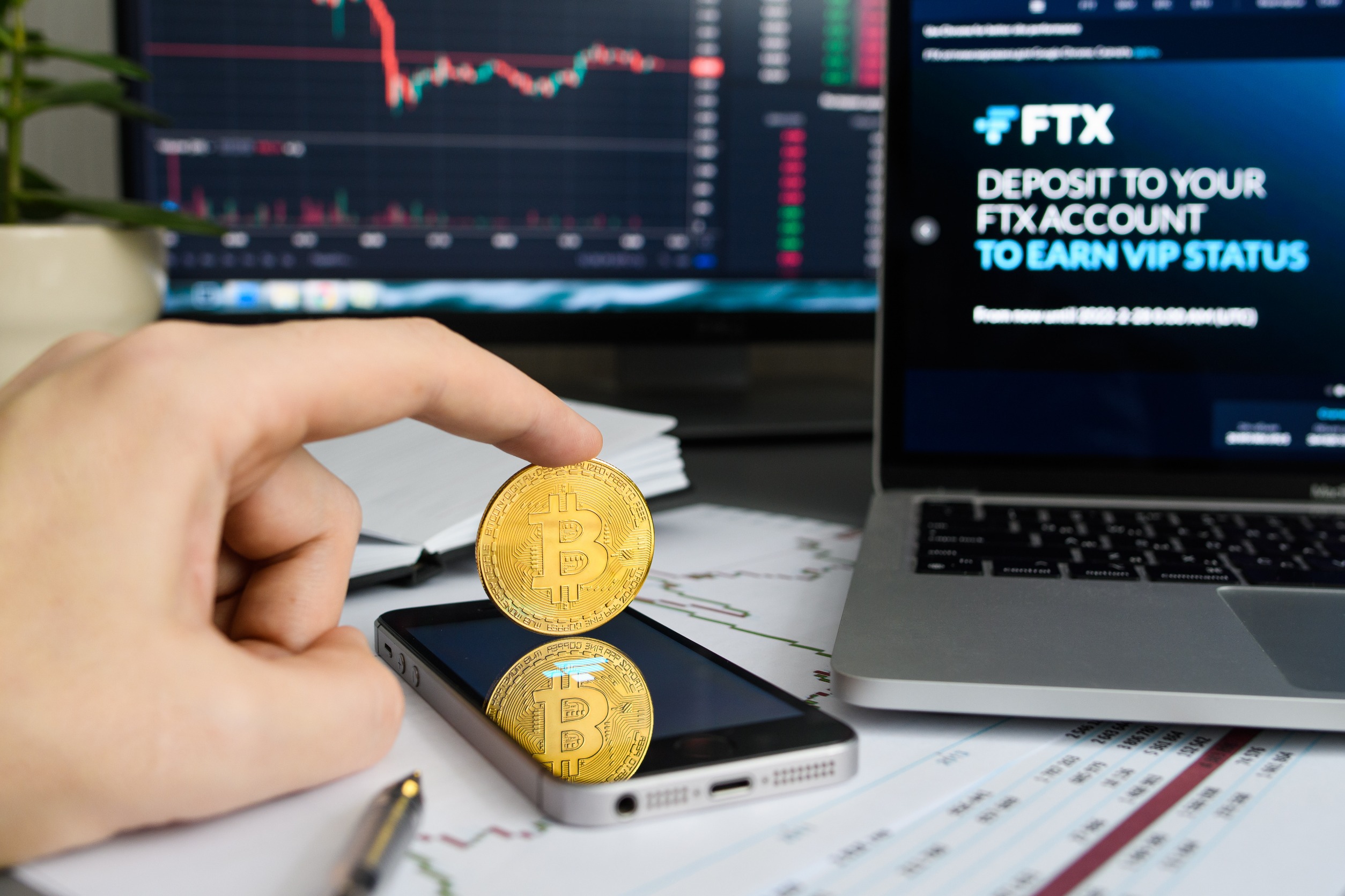 Finger keeping a coin in balance in front of a computer screen displaying "FTX"