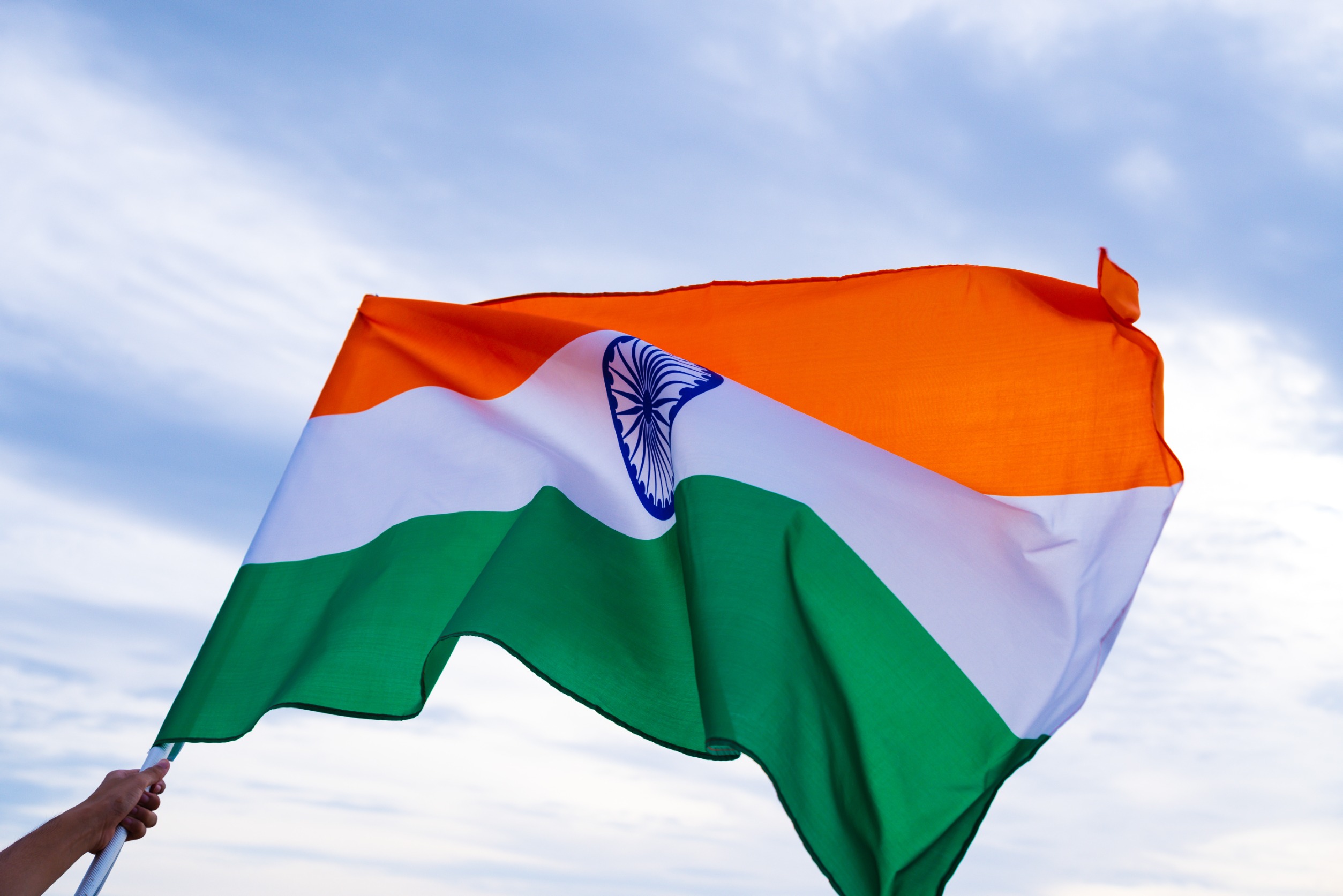Close up man hand holding India flag on the blue sky background. Indian Independence Day, 15 August.