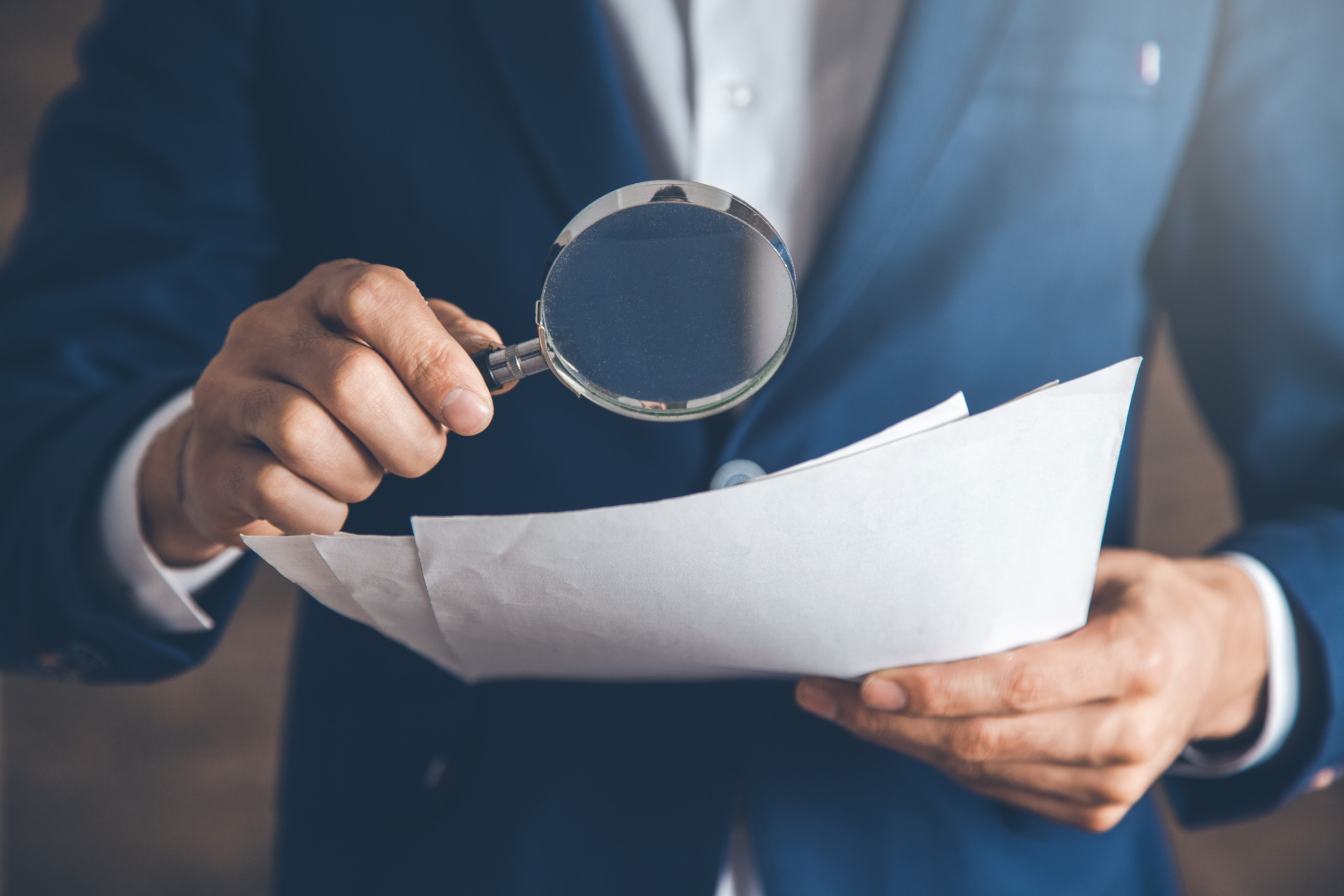 Man in a suit looking at pieces of paper through a magnifying glass