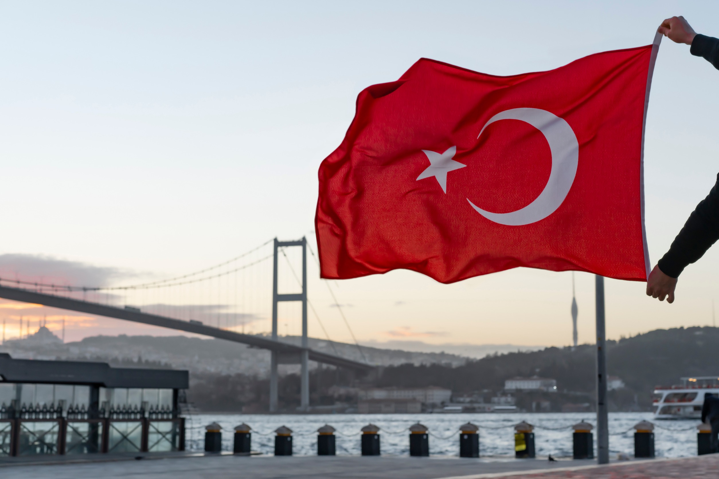 Man silhouette hold Turkish Flag in front of 15th July Martyrs Bridge (in Turkish 15 Temmuz Sehitler Koprusu) or Bosphorus Bridge in Istanbul, Turkey. Patriotism concept.