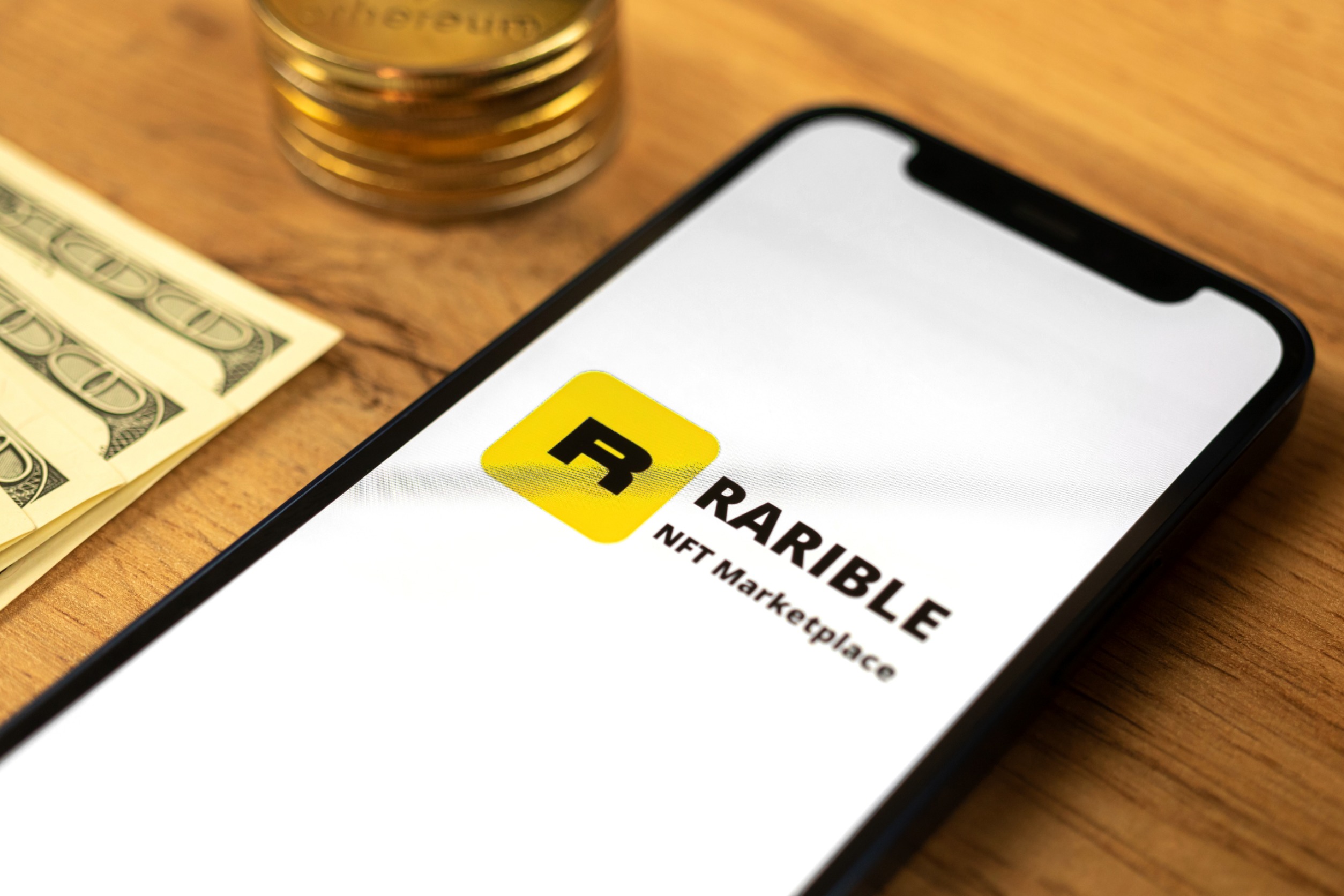 "Rarible" on a phone screen on a desk next to cash