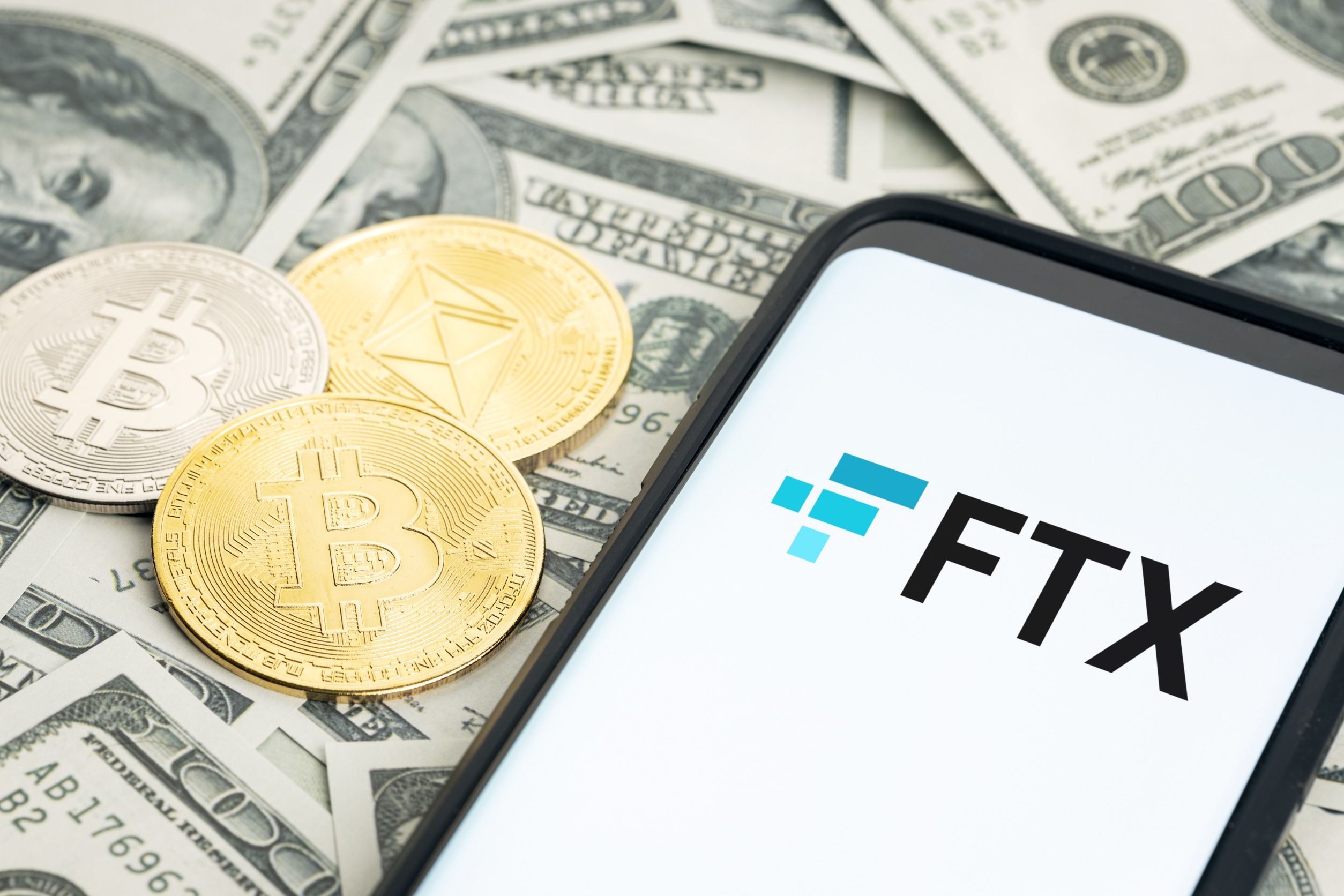 "FTX" on a phone screen on a pile of money.