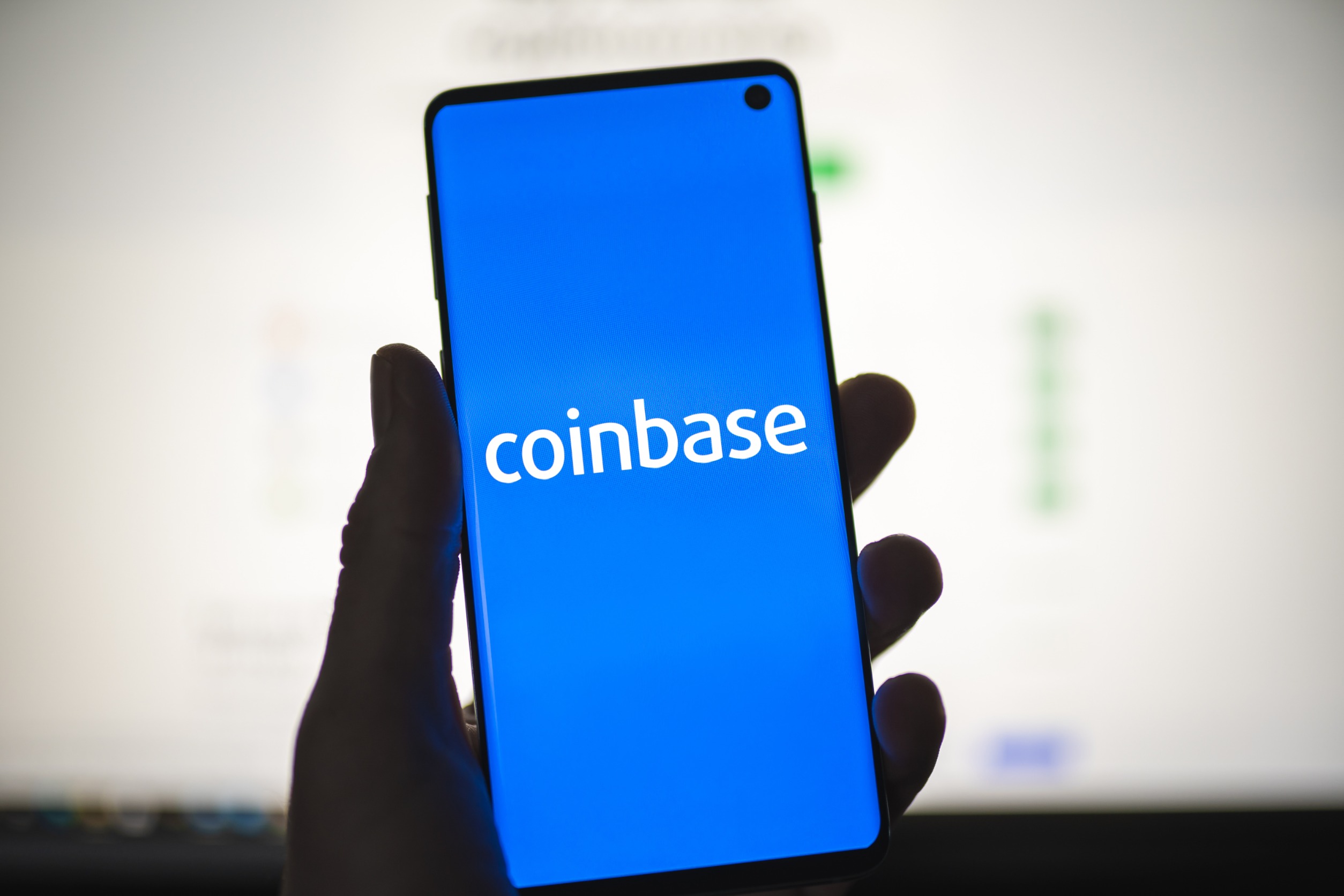 Man holding a smartphone with Coinbase logo with blurred website as background. Cryptocurrency exchange, trading platform