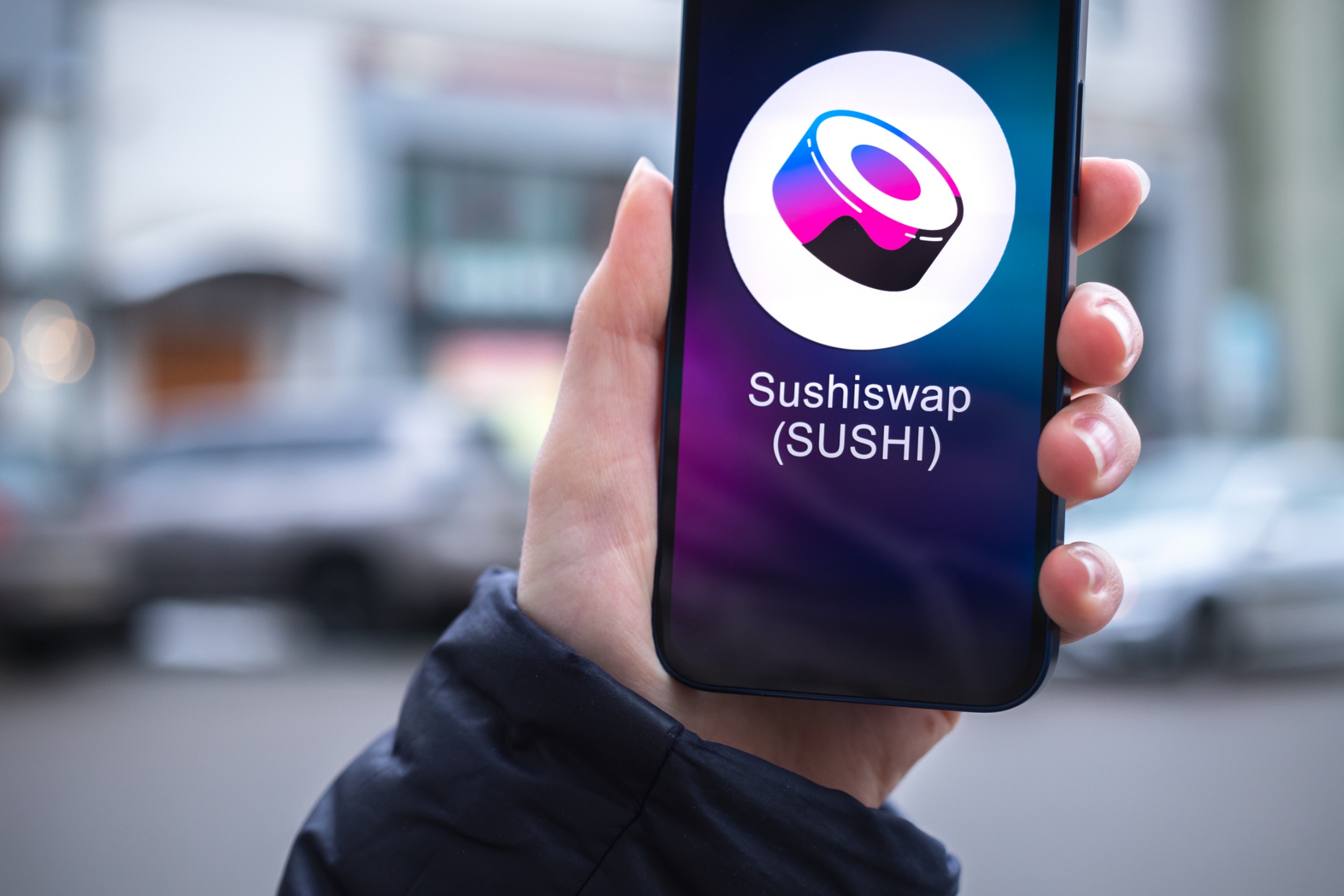 hand holding a smartphone that is displaying "Sushiswap(SUSHI)".