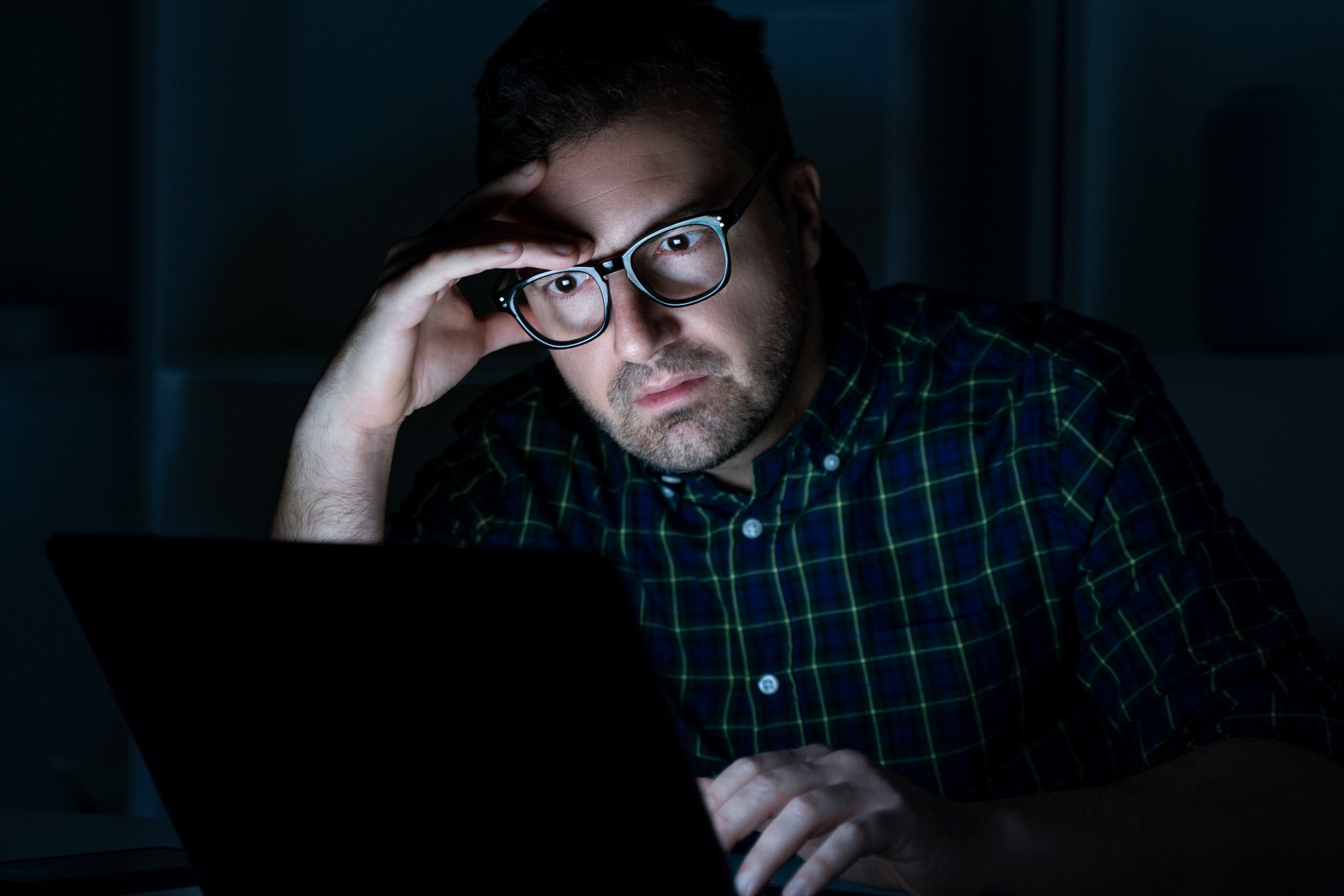 A worried man in a dark room in front of a computer