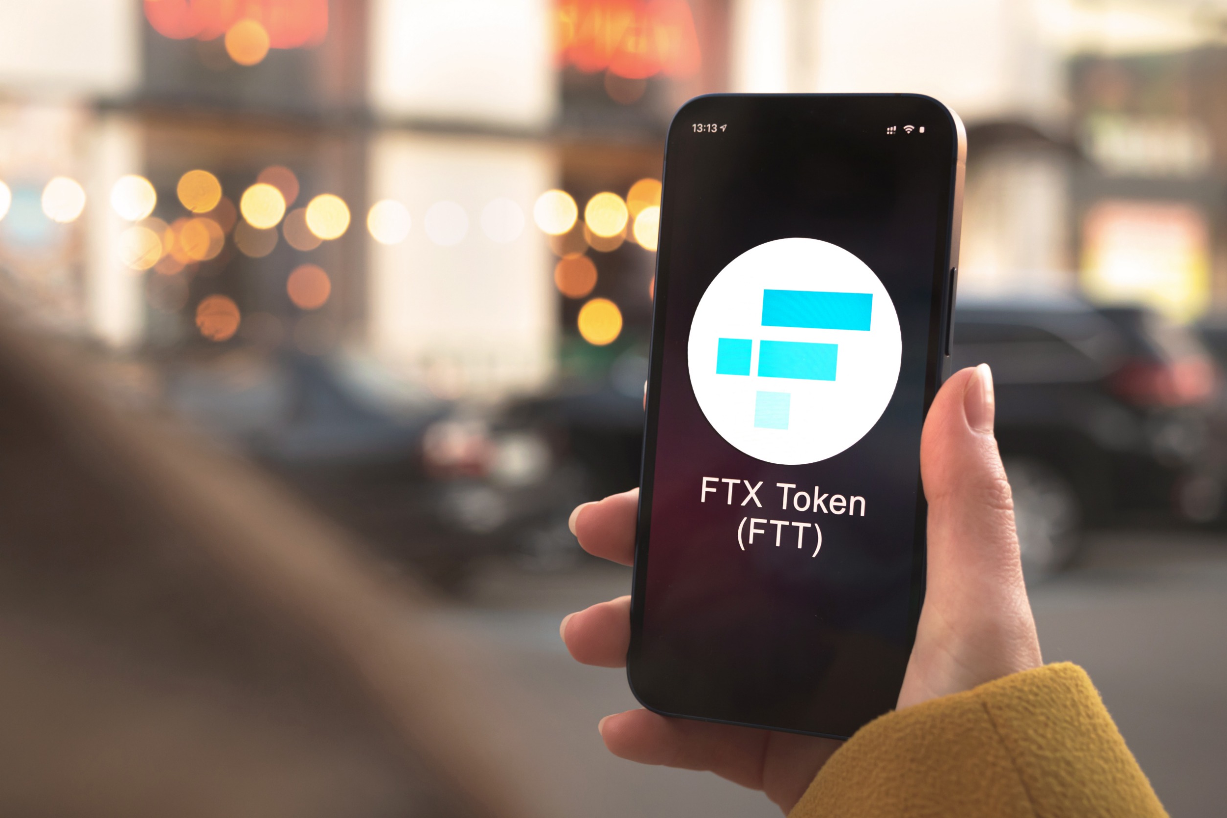 A hand holding a smartphone displaying "FTX Token (FTT)"