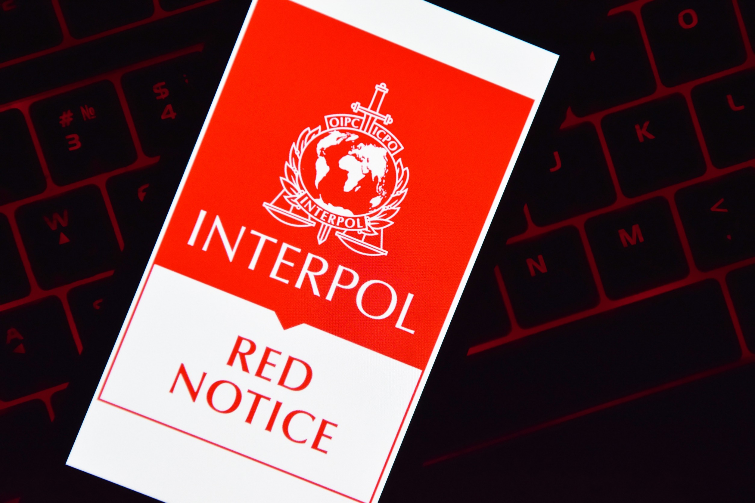 Smartphone laying on a keyboard and displaying "Interpol, Red Notice"