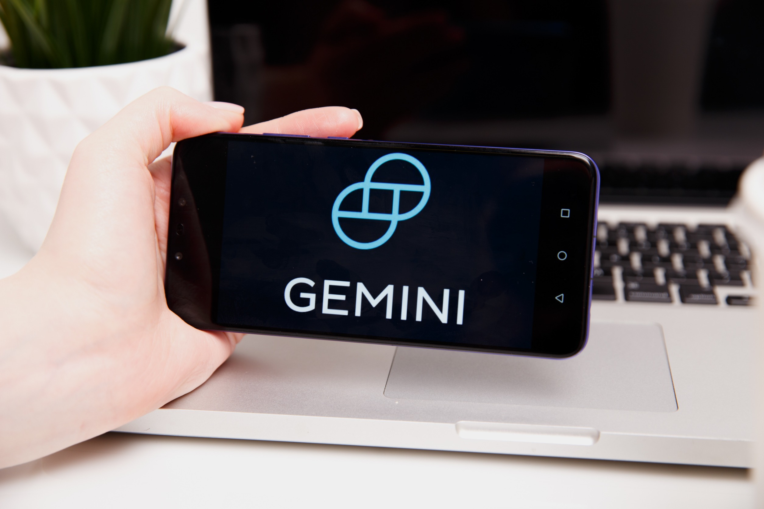 A smartphone displaying "Gemini" in front of a laptop.